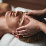 Femme allongée recevant un massage relaxant du visage, dans une ambiance calme et apaisante, illustrant la détente profonde, le relâchement des tensions et le bien-être naturel de ce soin manuel sans huile.