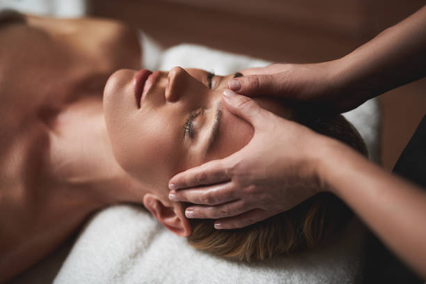 Femme allongée recevant un massage relaxant du visage, dans une ambiance calme et apaisante, illustrant la détente profonde, le relâchement des tensions et le bien-être naturel de ce soin manuel sans huile.